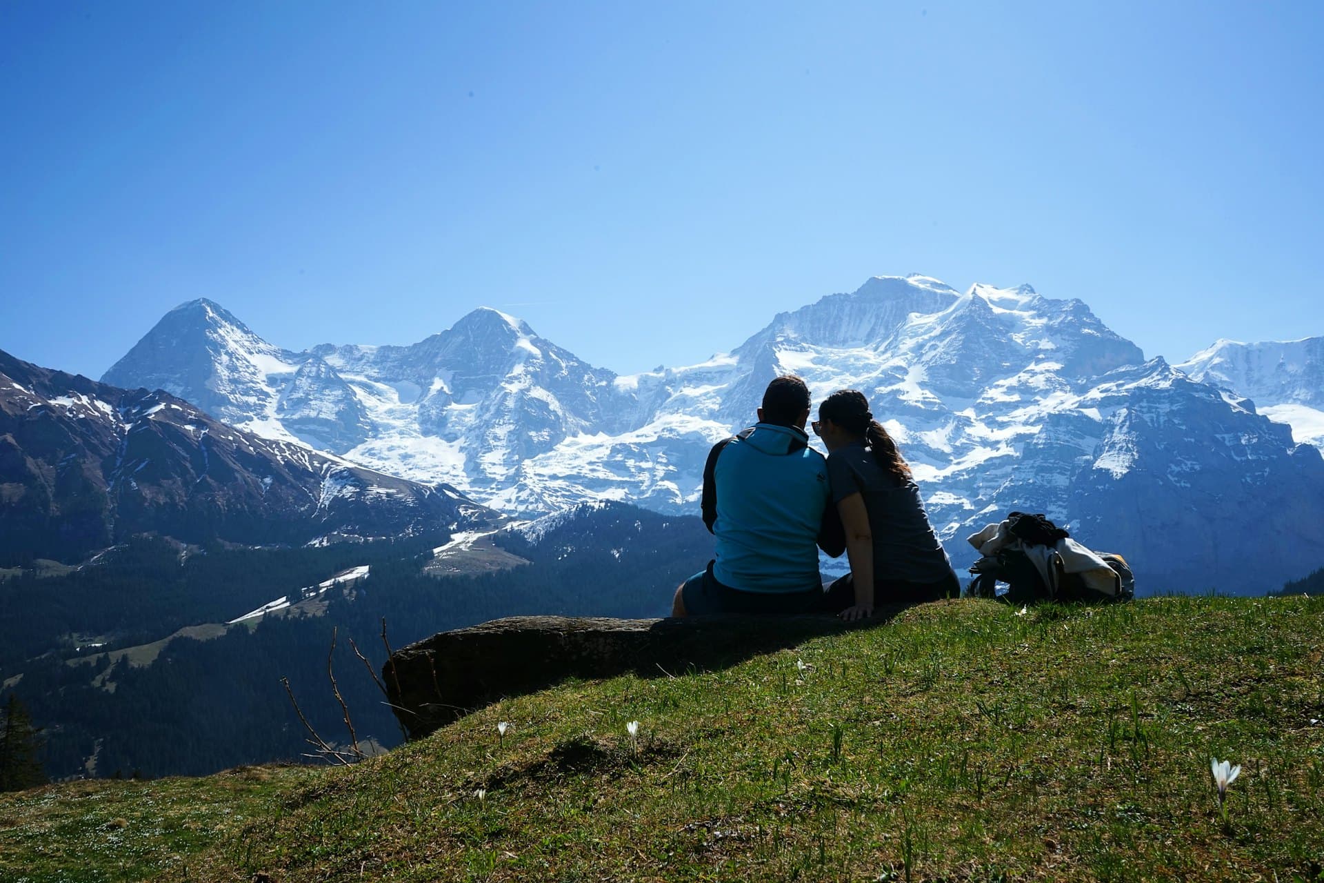 Un couple assis dans l'herbe face à des sommets enneigés