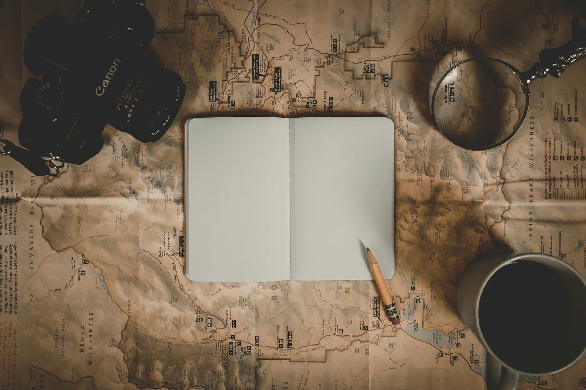 Un carnet ouvert posé sur une vieille carte, avec un appareil photo et une tasse de café