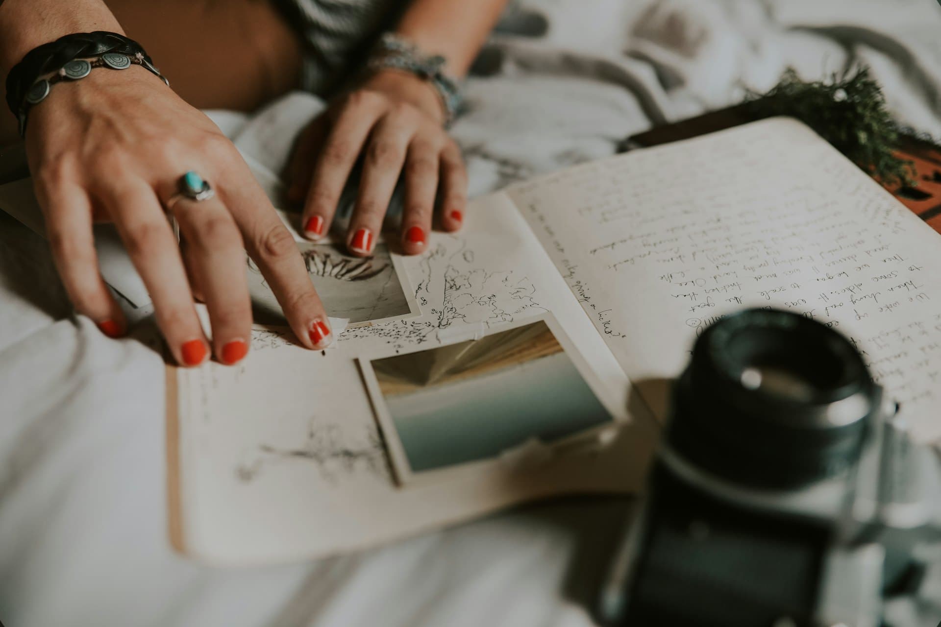 Des mains posées sur un carnet de voyage rempli de notes et de photos, à côté d'un appareil photo