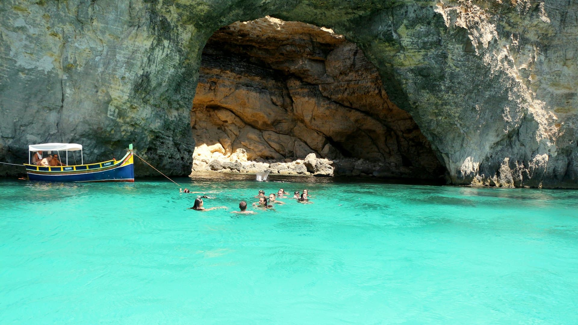 Des baigneurs dans une crique turquoise, près d'un bateau de pêcheurs