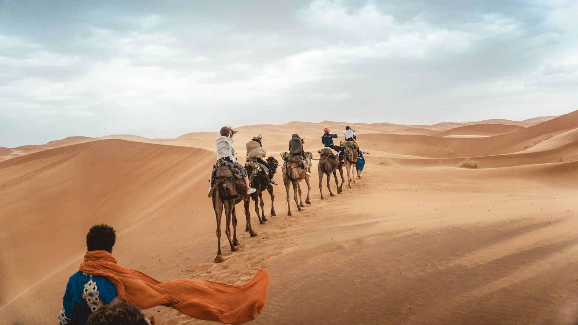 Une caravane de dromadaires dans les dunes, un voyageur au foulard orange au premier plan