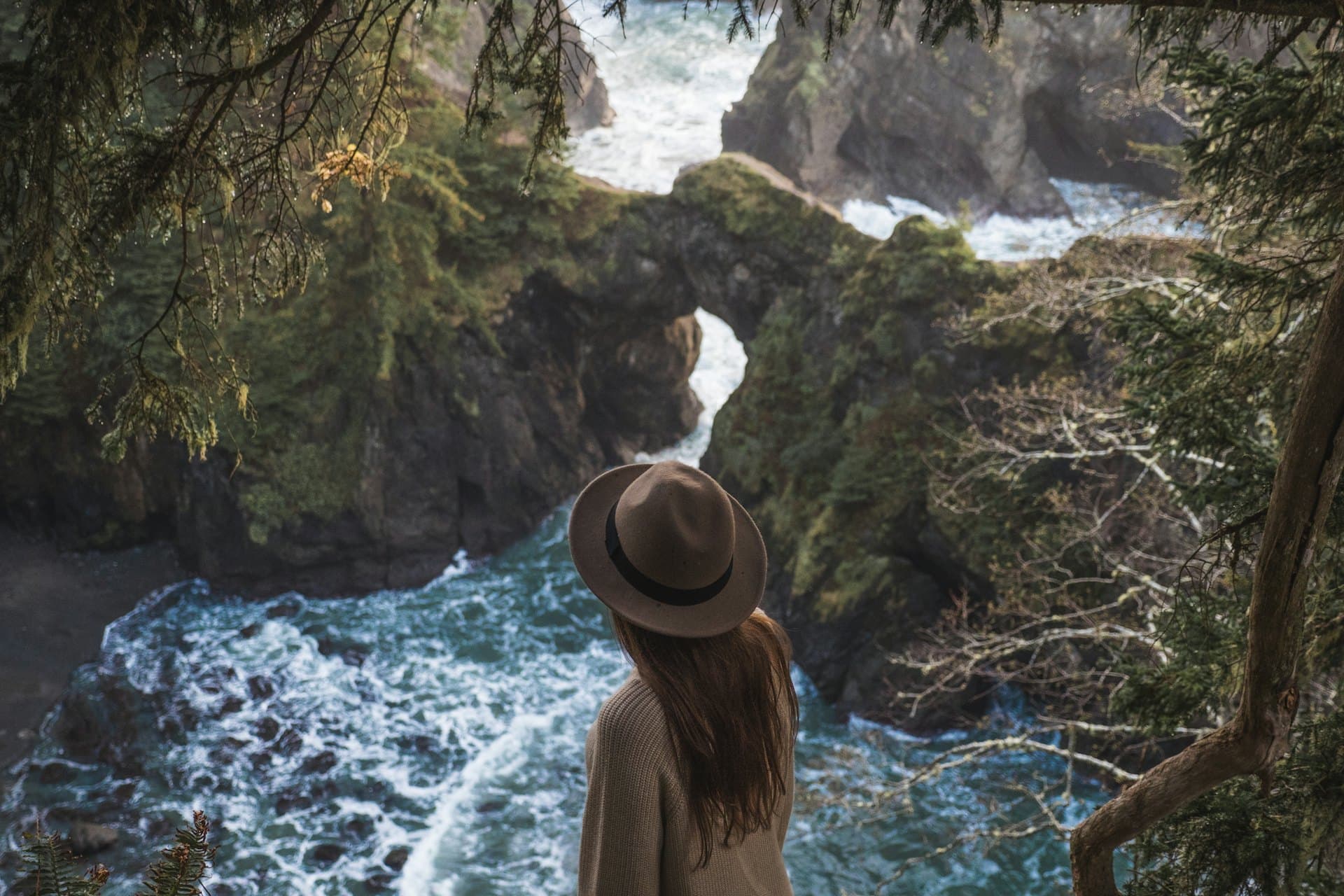 Une voyageuse au chapeau contemple des falaises couvertes de verdure au-dessus de la mer