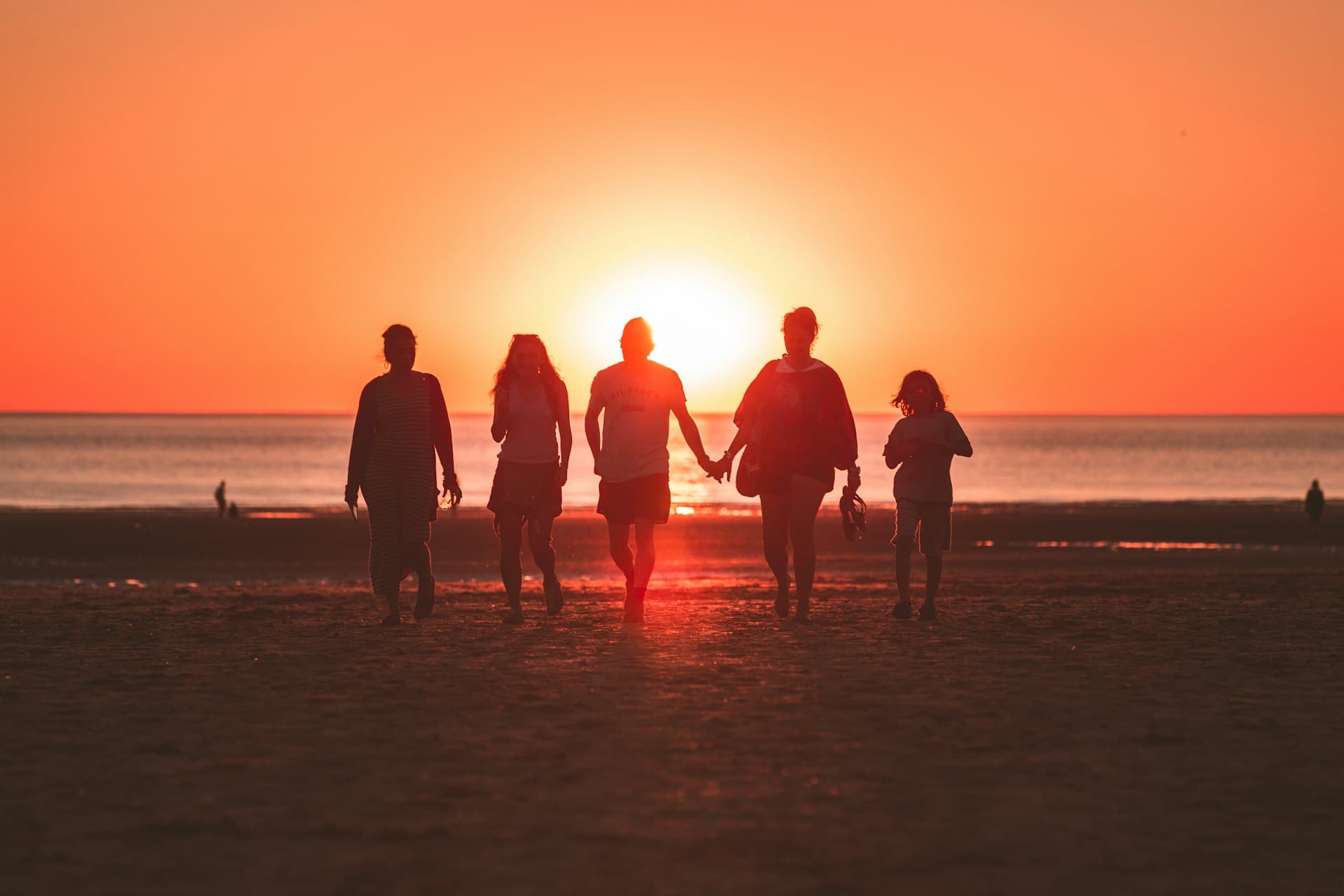 Une famille marche main dans la main sur une plage au coucher du soleil