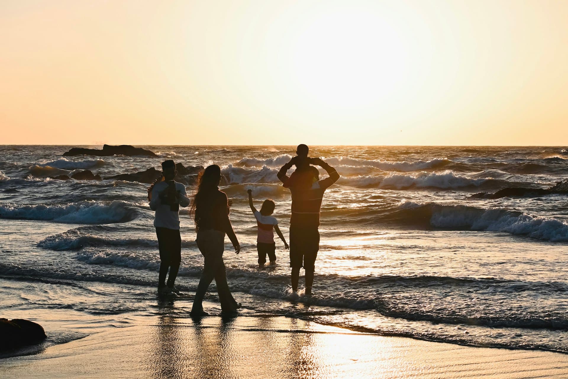 Une famille au bord des vagues, un enfant sur les épaules de son père, au soleil couchant