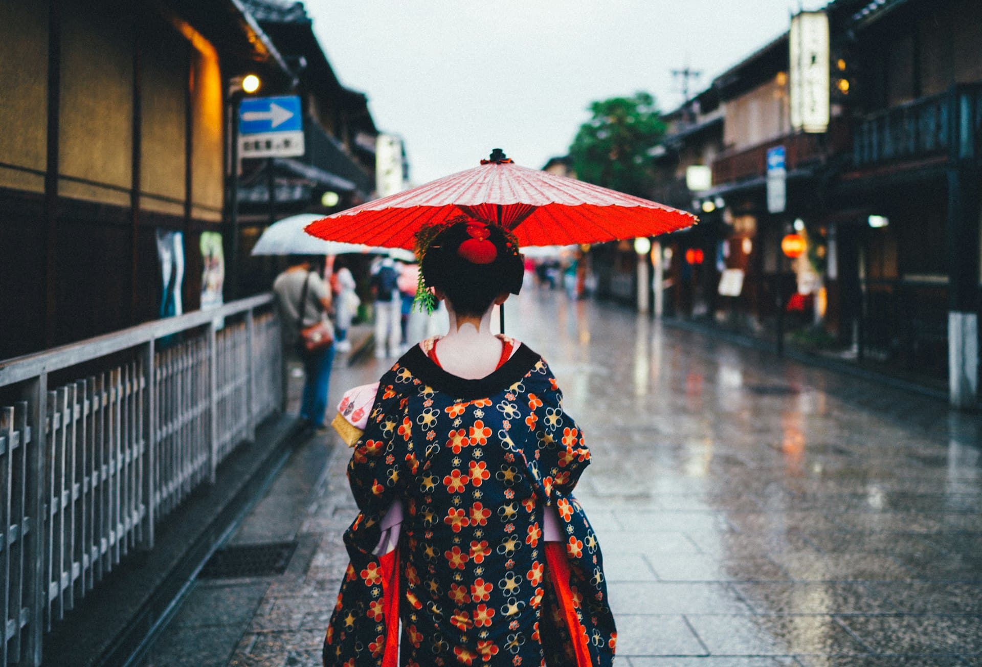 Une femme en kimono sous une ombrelle rouge dans une rue de Kyoto après la pluie