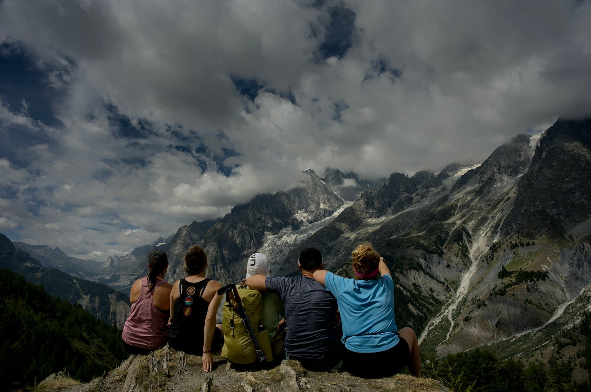 Cinq amis assis sur une crête rocheuse face à une vallée de montagne
