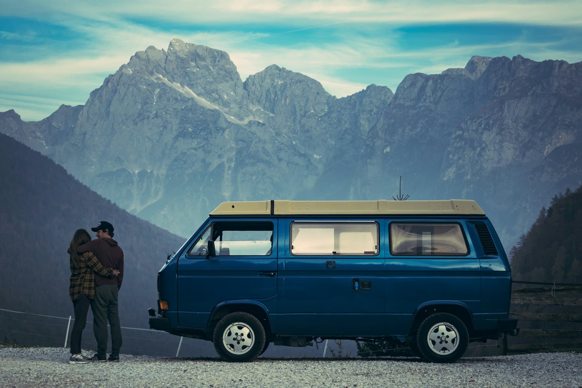 Un couple enlacé à côté d'un van bleu, au pied de montagnes
